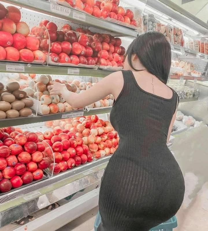 A woman in a black dress selecting fresh red apples from a supermarket display shelf