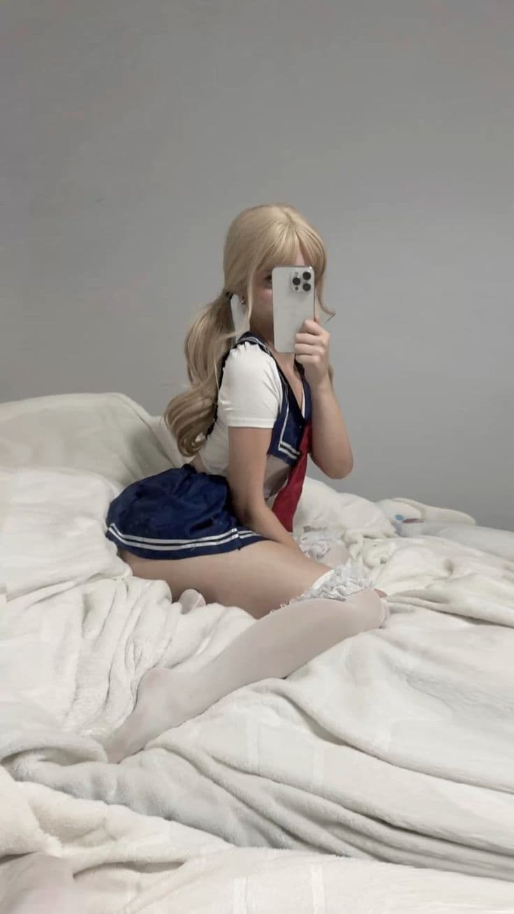 Blonde girl in sailor crop top taking mirror selfie on white bed