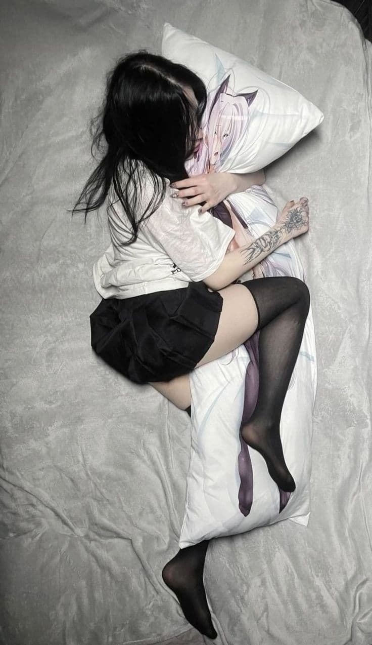 Girl in white top and black sheer stockings cuddling anime body pillow on bed