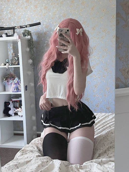Pink-haired girl in white crop top and black mini skirt with thigh-high stockings on bed