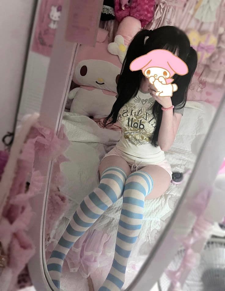 Girl in graphic tee and blue-white striped thigh-high socks in kawaii pink bedroom