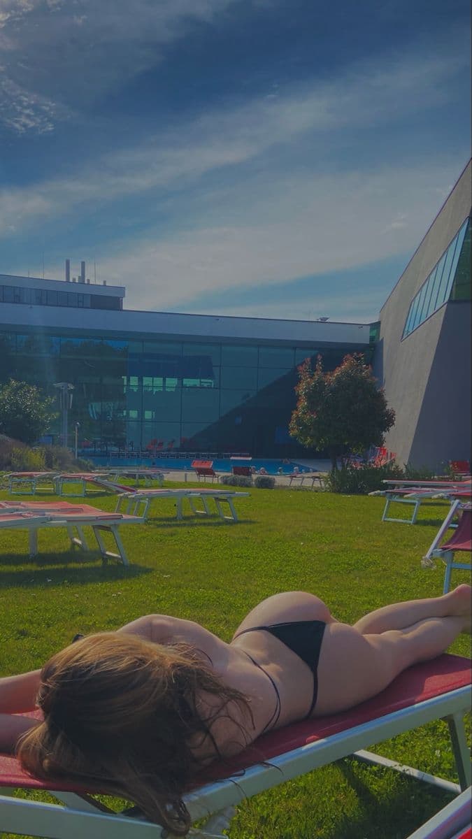 Woman in a black bikini lying face down on a sun lounger on a green lawn